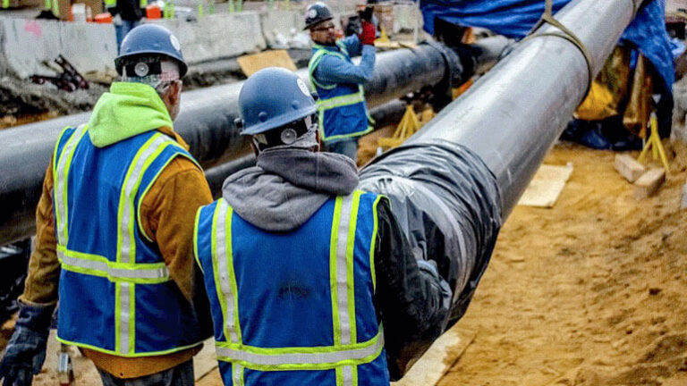 Workers in safety vests preparing pipes for laying during the construction of Terminal B