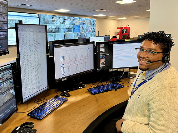 Smiling man wearing a headset sitting in front of multiple computer monitors at a desk