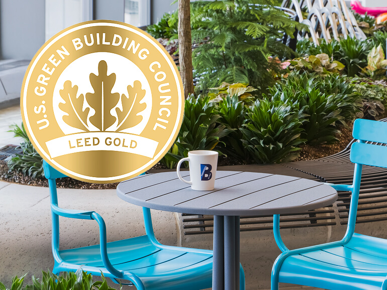 A Terminal B branded coffee mug sitting on an outdoor cafe table and an U.S. Green Building Council Leed Gold logo in the upper left